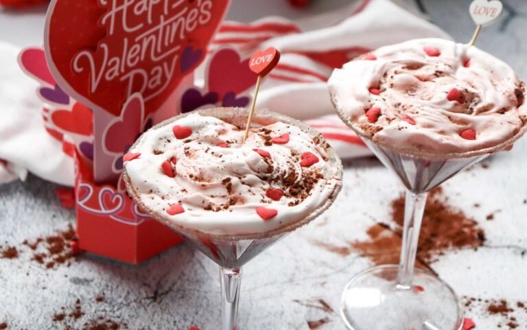 Two red velvet martini mocktails topped with whipped cream and heart sprinkles beside a Valentine’s Day card.