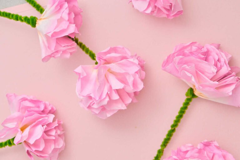 Pink Coffee Filter Flowers craft scattered with green pipe cleaner stems on a pastel background.