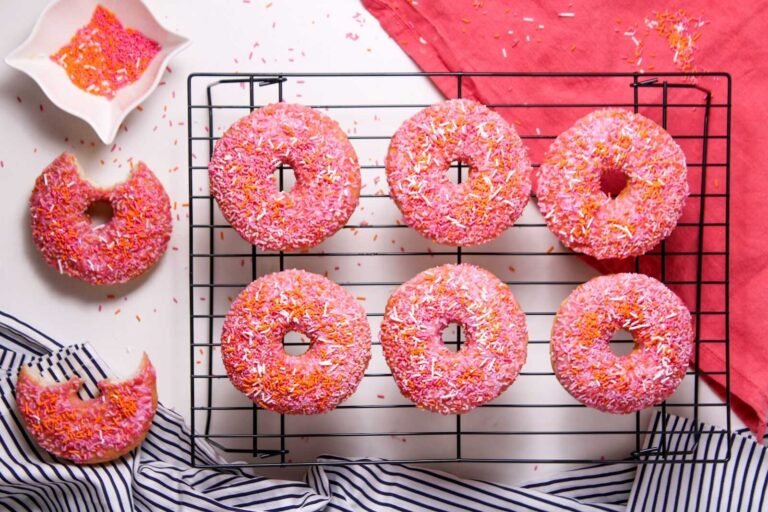 Overhead view of homemade glazed sprinkle donuts with pink icing on a cooling rack.