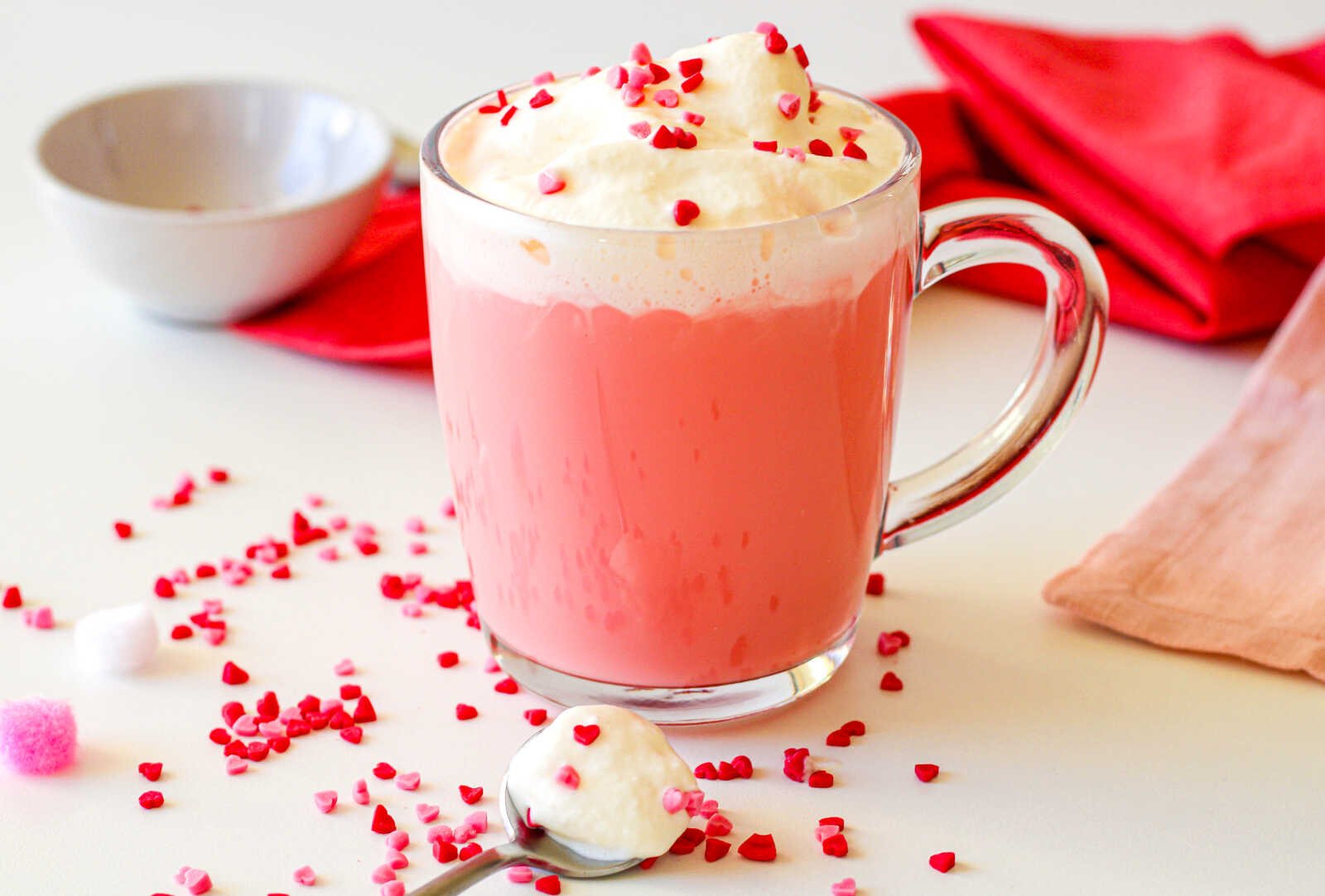 Red velvet hot chocolate with whipped cream and heart sprinkles in a glass mug.