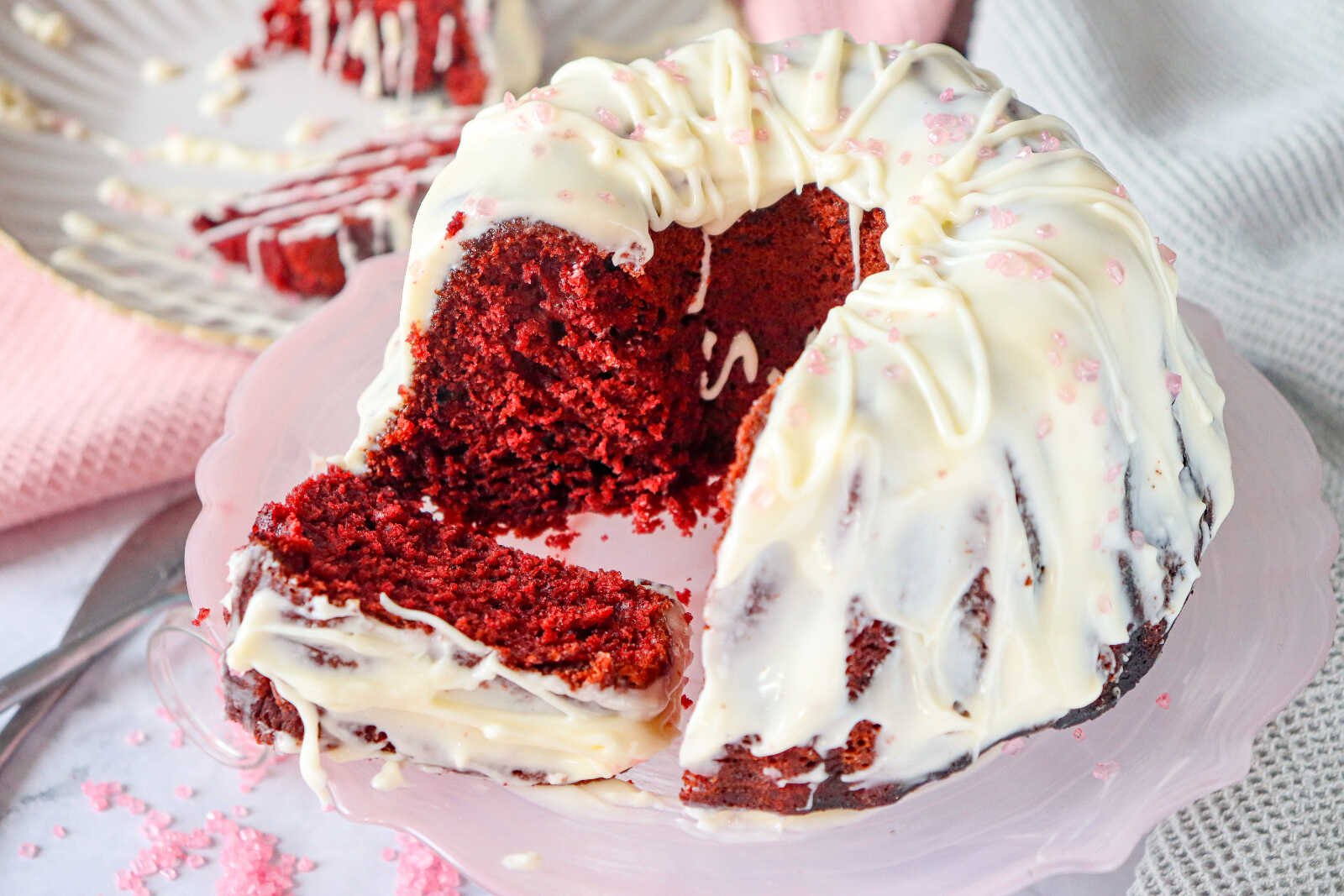 Red velvet bundt cake with cream cheese frosting and a slice removed on a serving plate.
