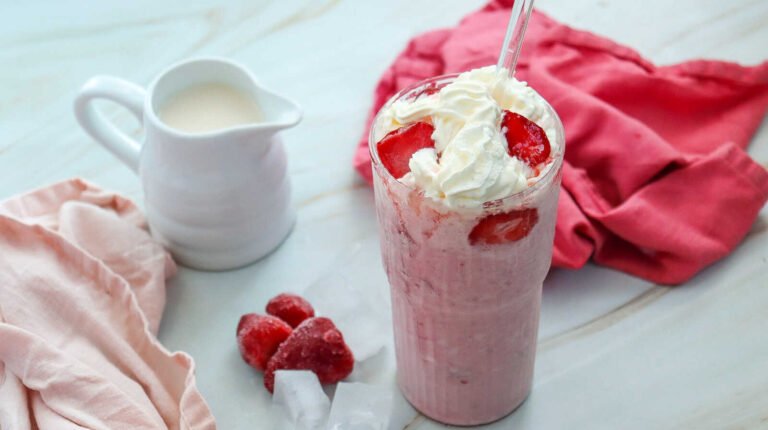 Starbucks copycat Strawberry Cheesecake Frappuccino topped with whipped cream and fresh strawberries in a tall glass.